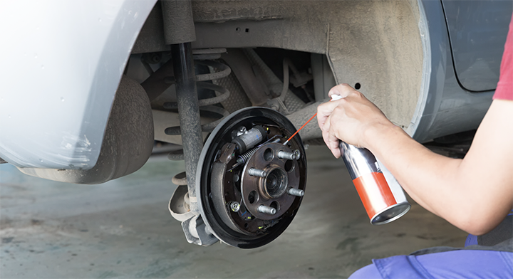 Person applying brake cleaner to a car&rsquo;s brake assembly during maintenance.