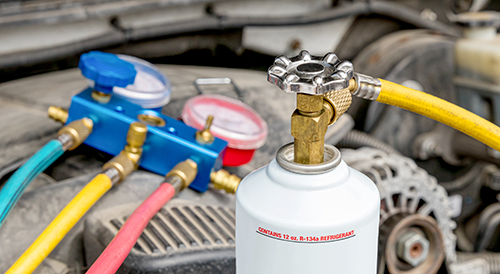 Automotive air conditioning refrigerant canister connected to manifold gauges under a vehicle hood.